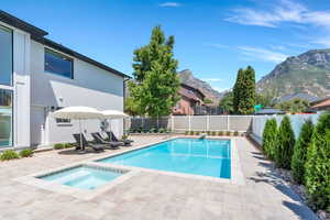 View of pool with a patio area, a fenced backyard, an in-ground hot tub, a diving board, and a mountain view