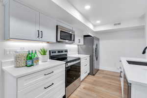 Kitchen with stainless steel appliances, light wood-type flooring, light countertops, white cabinets, and recessed lighting