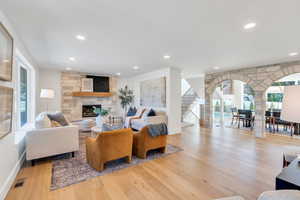Living room with arched walkways, wood finished floors, a stone fireplace, recessed lighting, and stairs