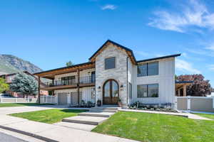 View of front of property featuring board and batten siding, a balcony, a gate, concrete driveway, and stone siding