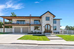 View of front of home with stone siding, board and batten siding, a balcony, french doors, and concrete driveway