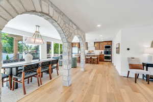 Dining room featuring light wood finished floors, recessed lighting, arched walkways, and decorative columns