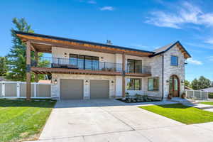 View of front of house with a balcony, stone siding, a gate, driveway, and board and batten siding