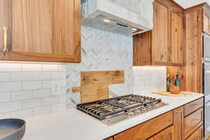 Kitchen featuring backsplash, ventilation hood, stainless steel gas stovetop, and light countertops