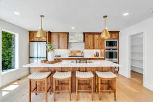 Kitchen featuring light wood-type flooring, stainless steel appliances, a center island with sink, light countertops, and recessed lighting