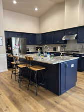 Kitchen featuring high vaulted ceiling, light stone countertops, a kitchen breakfast bar, a large island, and blue cabinetry