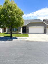 View of front of house with a garage, stone siding, driveway, stucco siding, and a front lawn