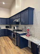 Kitchen with blue cabinets, appliances with stainless steel finishes and a high ceiling