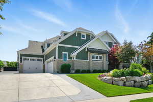 Craftsman house with a shingled roof, stone siding, board and batten siding, a garage, and a front lawn