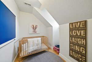 Bedroom featuring lofted ceiling, a textured ceiling, wood finished floors, and a crib