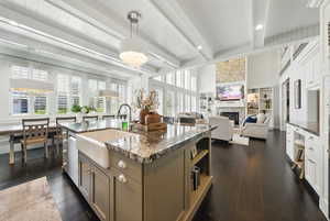 Kitchen featuring dark wood-type flooring, stone counters, beamed ceiling, a fireplace, and hanging light fixtures