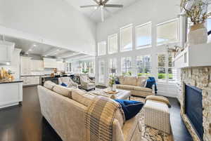 Living room featuring dark wood-type flooring, a ceiling fan, healthy amount of natural light, a fireplace, and a towering ceiling