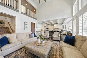 Living area featuring dark wood-style flooring, ceiling fan, stairs, and a towering ceiling