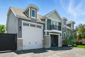 View of front of home featuring a balcony, stone siding, driveway, roof with shingles, and stucco siding