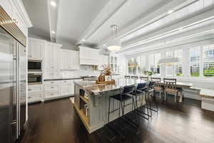 Kitchen featuring built in appliances, recessed lighting, a breakfast bar, light stone countertops, and white cabinets