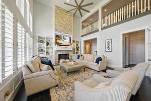 Living room with a towering ceiling, ceiling fan, dark wood-type flooring, a stone fireplace, and recessed lighting
