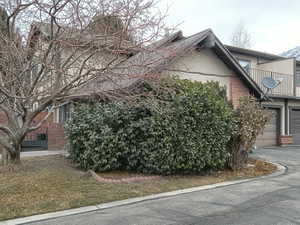 View of property exterior featuring brick siding, a balcony, a garage, and asphalt driveway