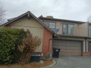 Back of property with a balcony, brick siding, asphalt driveway, and a garage