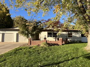 Front of home with a shaded front yard, bricked entrance, an attached garage, and concrete driveway