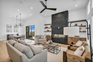 Living room with light wood finished floors, a chandelier, a high ceiling, a ceiling fan, and a tile fireplace