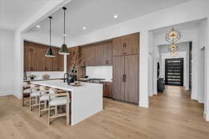 Kitchen with light countertops, a center island with sink, light wood-style floors, a kitchen breakfast bar, and recessed lighting