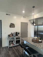 Kitchen featuring a kitchen bar, stainless steel fridge, dark wood-style flooring, a textured ceiling, and light stone countertops