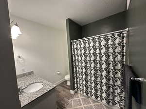 Full bath featuring a textured ceiling, vanity, a shower with curtain, and dark wood finished floors