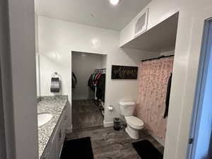 Full bathroom featuring vanity, wood finished floors, a walk in closet, a textured ceiling, and curtained shower