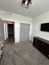 Carpeted bedroom featuring a textured ceiling and a closet