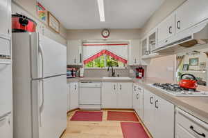 Kitchen with white appliances, light countertops, light wood-style flooring, white cabinetry, and under cabinet range hood