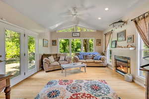 Living area featuring vaulted ceiling, ceiling fan, a glass covered fireplace, light wood-style flooring, and recessed lighting
