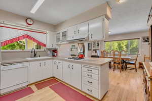 Kitchen featuring white appliances, light countertops, light wood-style floors, a peninsula, and a textured ceiling