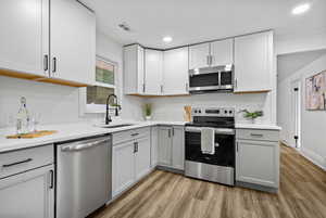 Kitchen with appliances with stainless steel finishes, light wood finished floors, light countertops, recessed lighting, and gray cabinetry