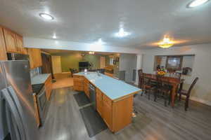 Kitchen with a textured ceiling, appliances with stainless steel finishes, light countertops, light wood-style floors, and a center island with sink