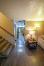 Hallway with a textured ceiling, dark wood-type flooring, and stairs