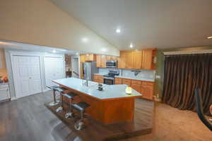Kitchen featuring appliances with stainless steel finishes, an island with sink, light countertops, a kitchen breakfast bar, and recessed lighting