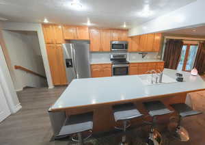 Kitchen featuring appliances with stainless steel finishes, a textured ceiling, a kitchen breakfast bar, wood finished floors, and light countertops