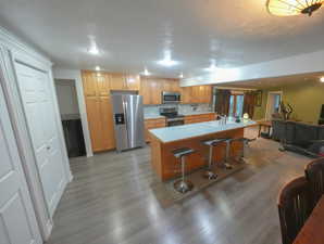 Kitchen with stainless steel appliances, a textured ceiling, light countertops, open floor plan, and light wood-style flooring