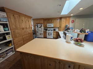 Kitchen featuring a skylight, light countertops, white appliances, recessed lighting, and a peninsula