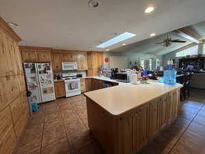 Kitchen featuring a skylight, tile patterned floors, white appliances, a peninsula, and light countertops