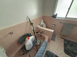 Full bath featuring tile walls, wainscoting, and a bath