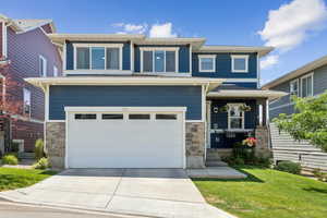 View of front of property featuring stone siding, a garage, driveway, and a front lawn