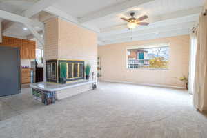 Unfurnished living room with brick wall, a fireplace, healthy amount of natural light, a wooden ceiling with exposed beams, and light carpet