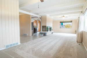 Unfurnished living room with a ceiling fan, wood walls, a large fireplace, brick wall, and light carpet