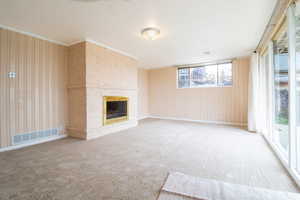Unfurnished living room with a brick fireplace, carpet floors, crown molding, and wooden walls