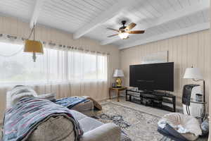 Carpeted living room with wood walls, ceiling fan, and a wooden ceiling with exposed beams