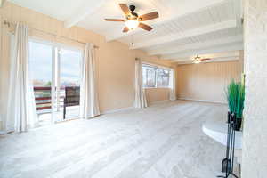 Carpeted spare room featuring wooden walls, ceiling fan, and a wooden ceiling with exposed beams
