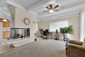 Living room with an office area, light colored carpet, brick wall, ceiling fan, and beamed ceiling