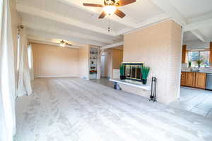 Unfurnished living room featuring wood walls, a fireplace, light colored carpet, built in features, and a ceiling fan