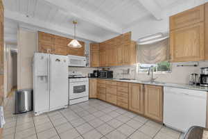 Kitchen featuring white appliances, light tile patterned flooring, decorative light fixtures, light stone countertops, and a wooden ceiling with exposed beams